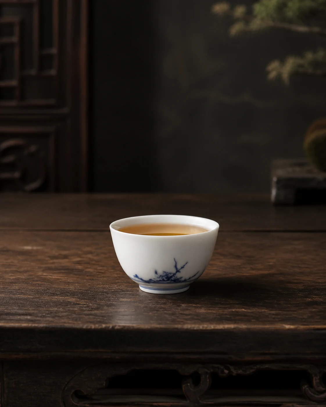 A blue-and-white gaiwan on its saucer with two cups of amber liquor beside it.