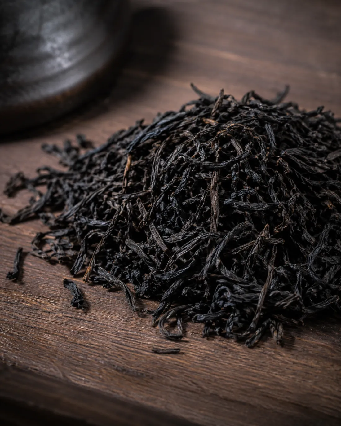 A heap of wiry, near-black tea leaf on a worn wooden board.