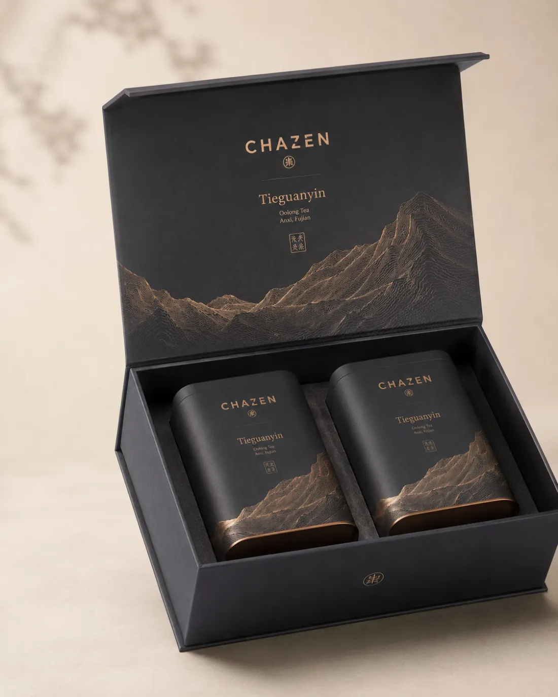 Open charcoal presentation box holding two matte black Tieguanyin tins against embossed bronze mountains